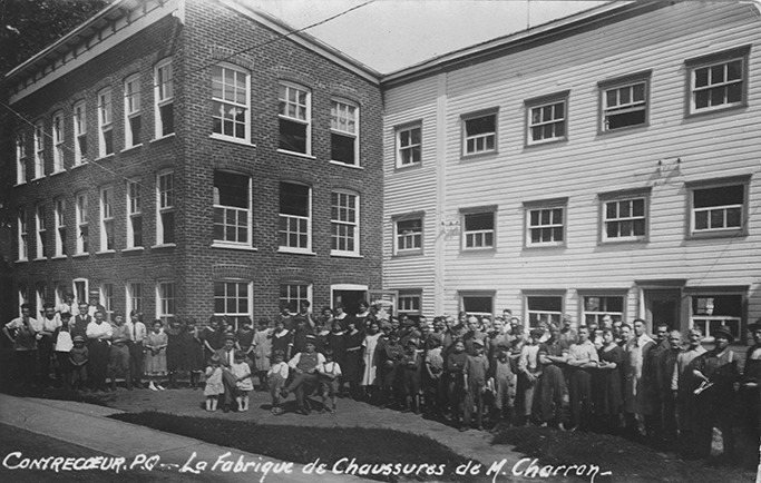 The photo shows Charron’s Shoe Mill employees assembled in front of the plant. We see that a new brick section has replaced the white wooden house that had been erected in front of the factory.