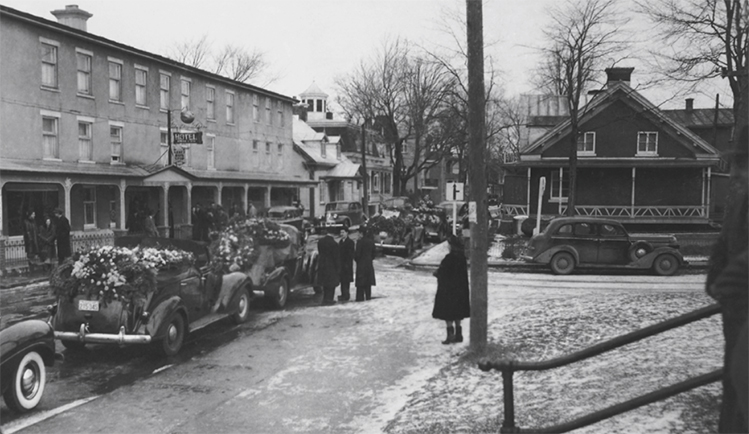 La photo, prise devant l’Hôtel de la Pomme d’or, montre un cortège de véhicules à l’occasion des funérailles de Léo Papin en 1948.