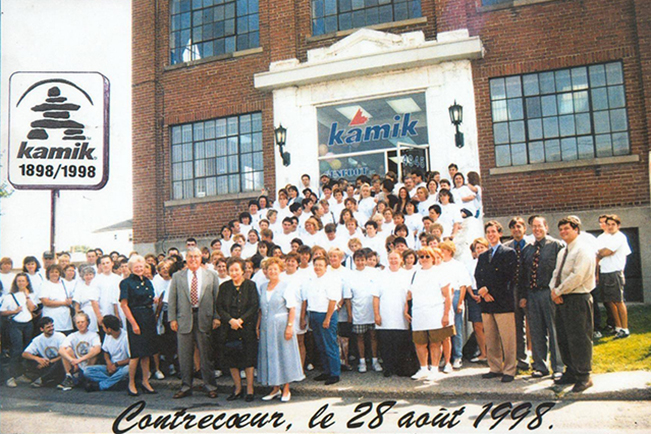 In this picture, we see all Kamik manufacturing employees gathered in front of the factory to celebrate the business’s 100th anniversary. They number over a hundred, mainly women, and they all wear a white shirt. In the front, on the right-hand side, we see members of the management team.