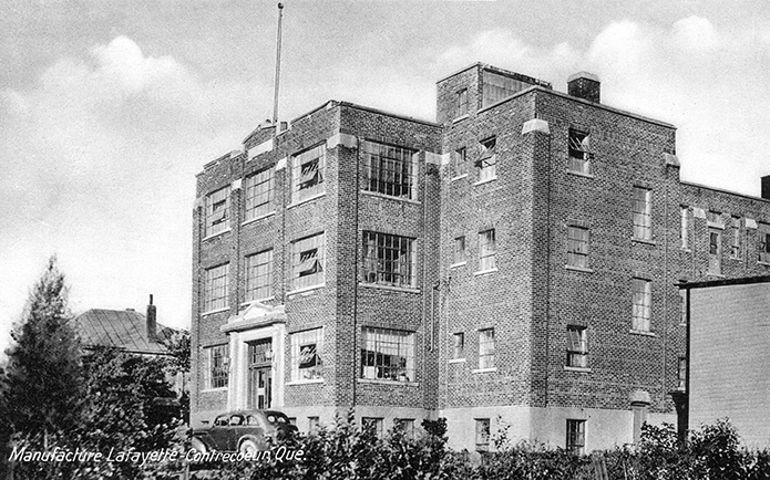 Photo taken from des Manufactures Street, showing Lafayette Shoes. We see the building’s façade and western side. One car is parked out front.