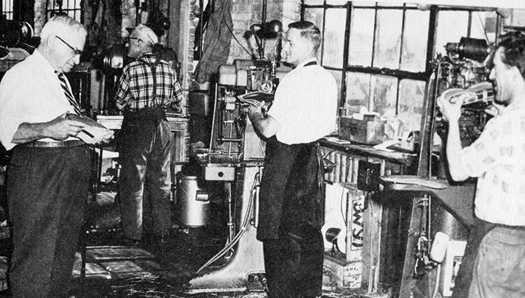 The photo shows Henri Bergeron, manager of operations at Lafayette from 1945 to 1960, inspecting a shoe being crafted at the assembly stage. Three workers, Jos Geoffrion, Jean-Paul Piché and Maurice Beauregard, are set up in front of their machines.