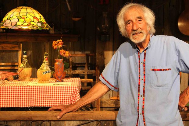 Color photo of Gilles Mathieu in front of a reproduction of a mezzanine of La Butte during the 2021 exhibition in Val-David.