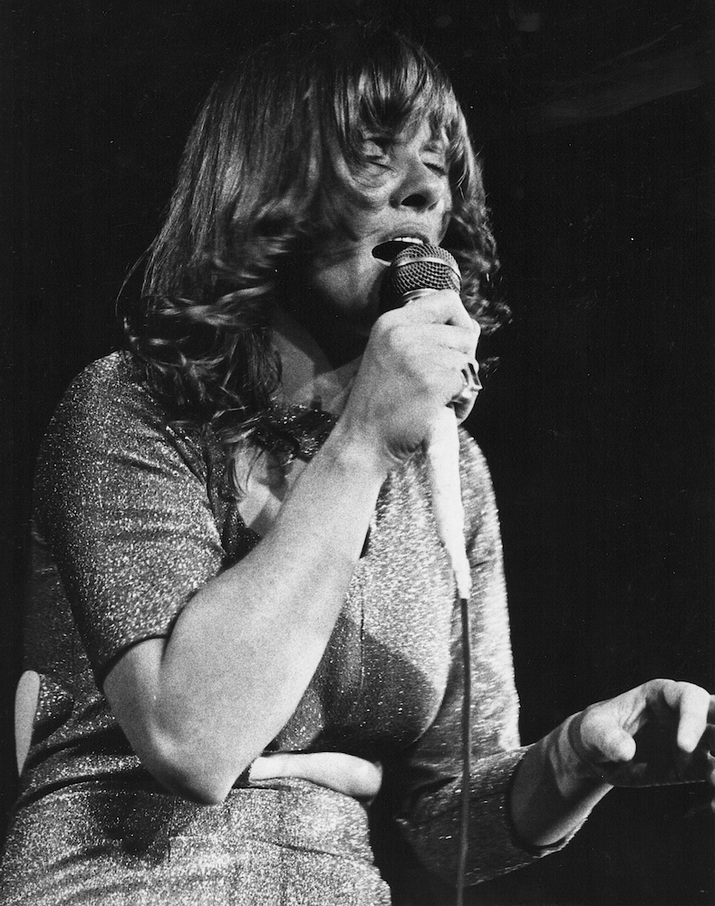 Black and white photo of Diane Dufresne singing with her eyes closed and holding a microphone to her mouth.