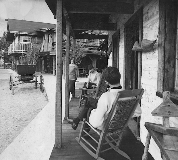 Black and white photo of three people sitting on the porch of a house in La Butte.