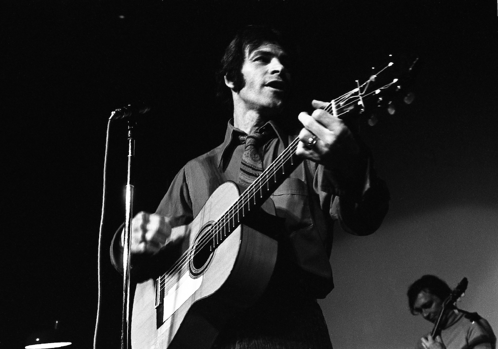 Black and white photo of Claude Gauthier performing holding his guitar.