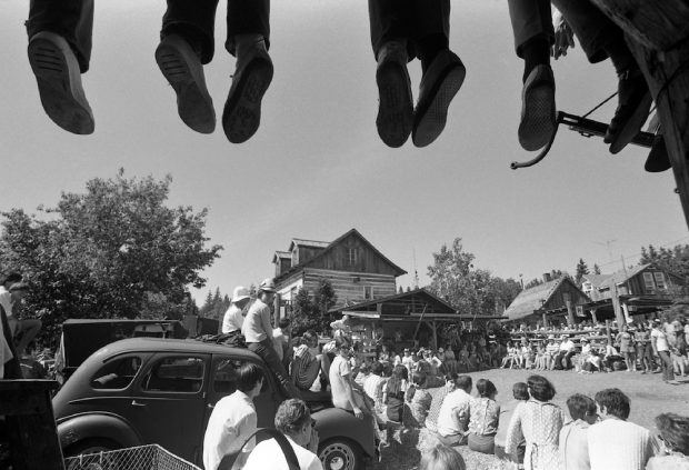 Black and white photo of about 100 spectators attending an outdoor performance at La Butte. At the top of the picture, the feet of people sitting on part of the roof of La Butte can be seen.
