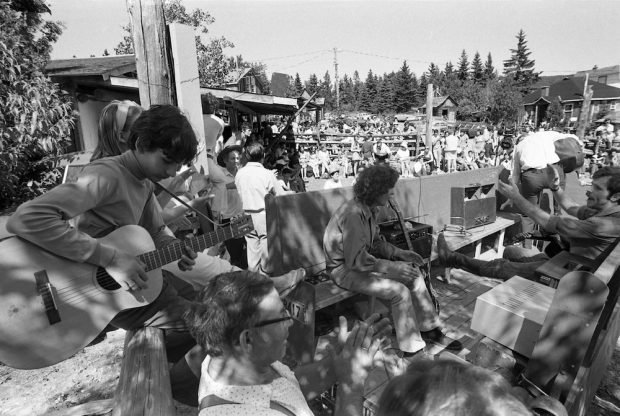 Black and white photo of about 100 spectators attending an outdoor performance at La Butte. At the top of the picture, the feet of people sitting on part of the roof of La Butte can be seen.