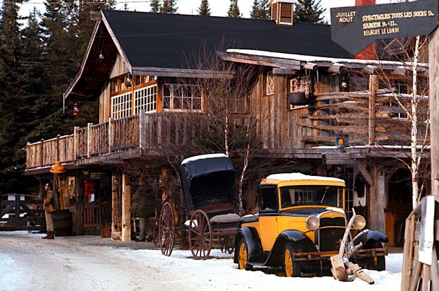 Colour photo of La Butte in winter. Wooden walls and large pane windows are predominant. An old, yellow, 1930s Ford truck is parked at the entrance.