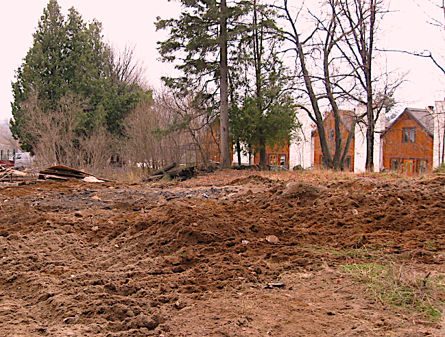Colour photo of the empty, bare ground after the demolition of La Butte on Monty Street in Val-David. In the distance, trees without leaves.