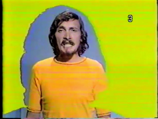Colour photo of Jacques Michel singing in a yellow sweater.
