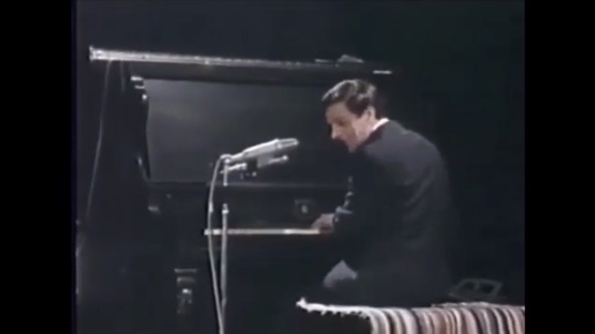 Colour photo of Claude Léveillée from behind, sitting at the piano.