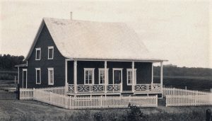 Black and white photo of a dark house encircled by a white fence.