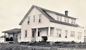 Black and white photo of a white house with nuns standing on the porch.