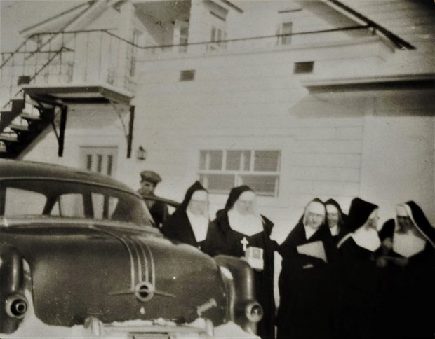 Group of nuns in front of a car.