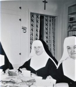 Black and white photo of two women in nun’s habits sitting around a table.