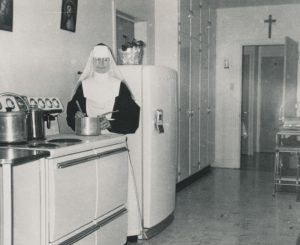 Black and white photo of a nun in a kitchen.