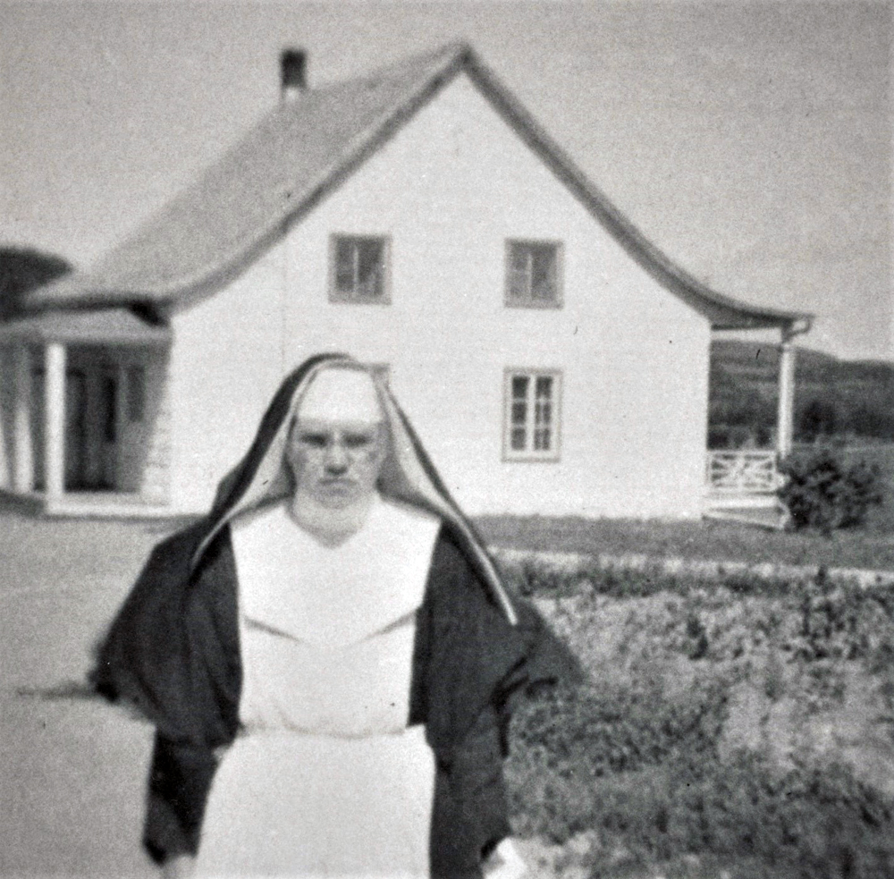 Black and white photo of a nun in front of a house.