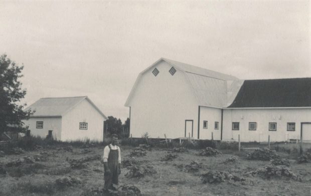 Black and white photo of a man in front of the farm abutting a field.