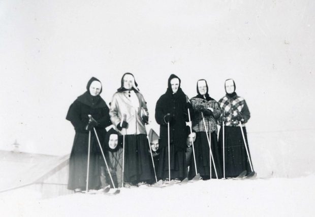 Black and white photo of five women wearing skis and three others kneeling in the snow. They are wearing veils and winter garb.