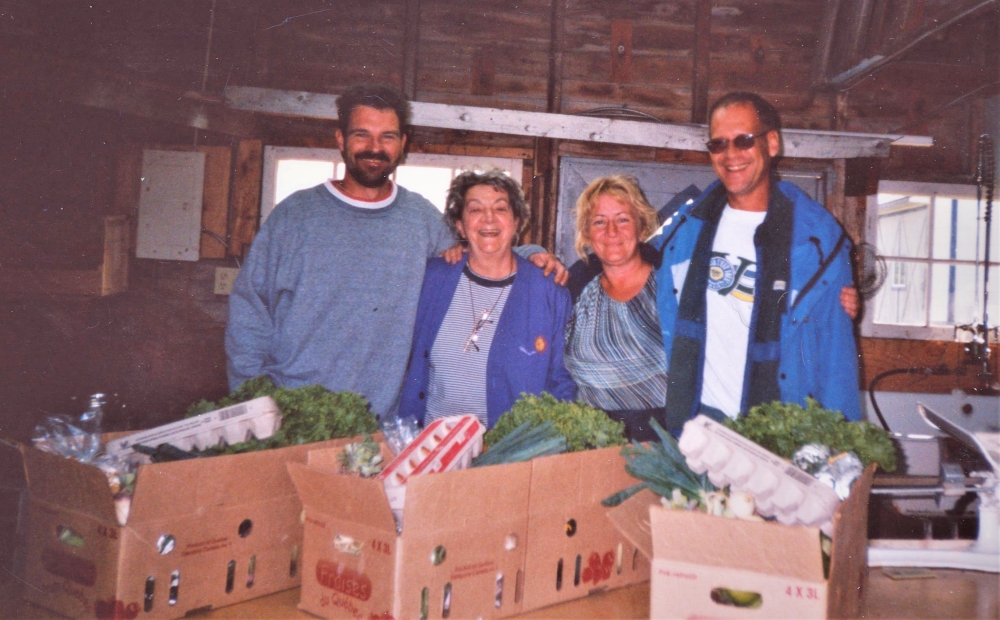 Colour photo of four farm employees receiving baskets filled with fresh vegetables and eggs.
