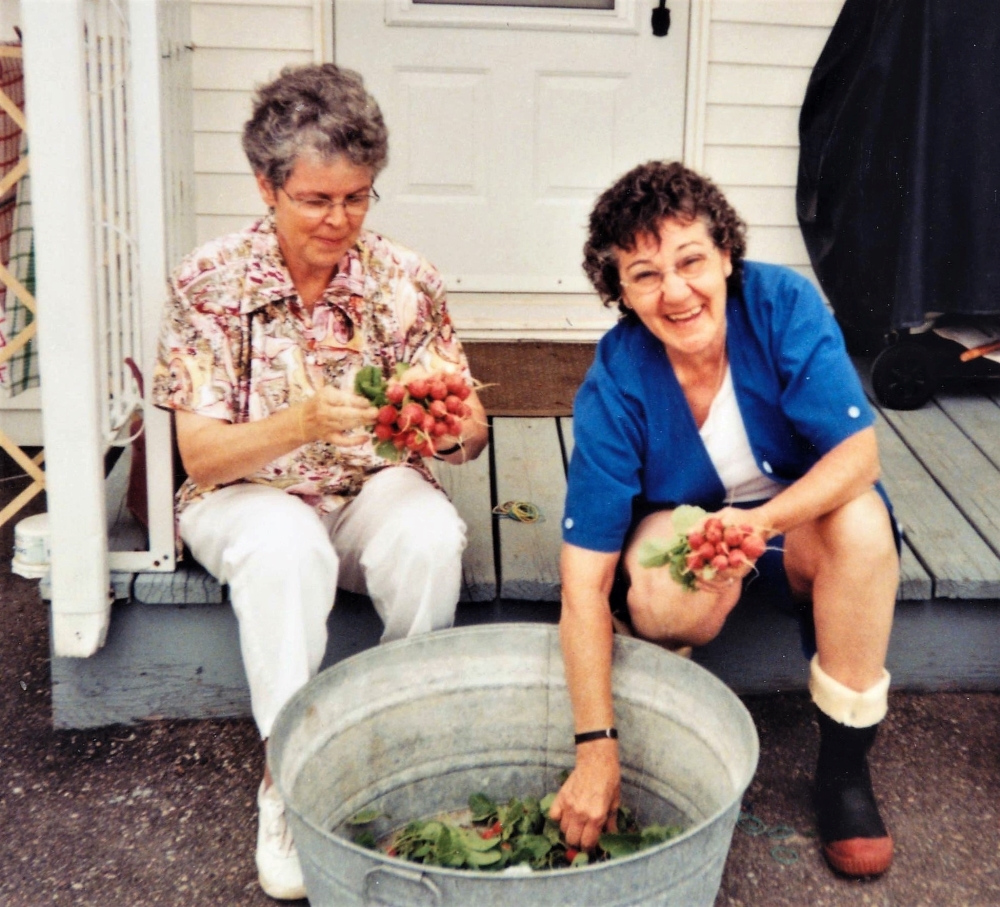Two women sitting on a porch and washing radish bunches.