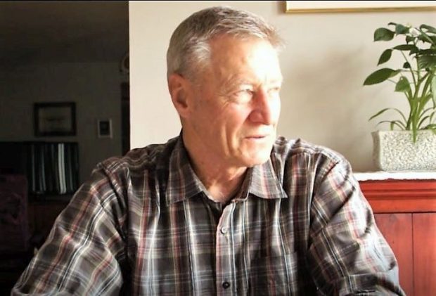 Close-up view of a man in a checkered shirt sitting behind a desk or a table.