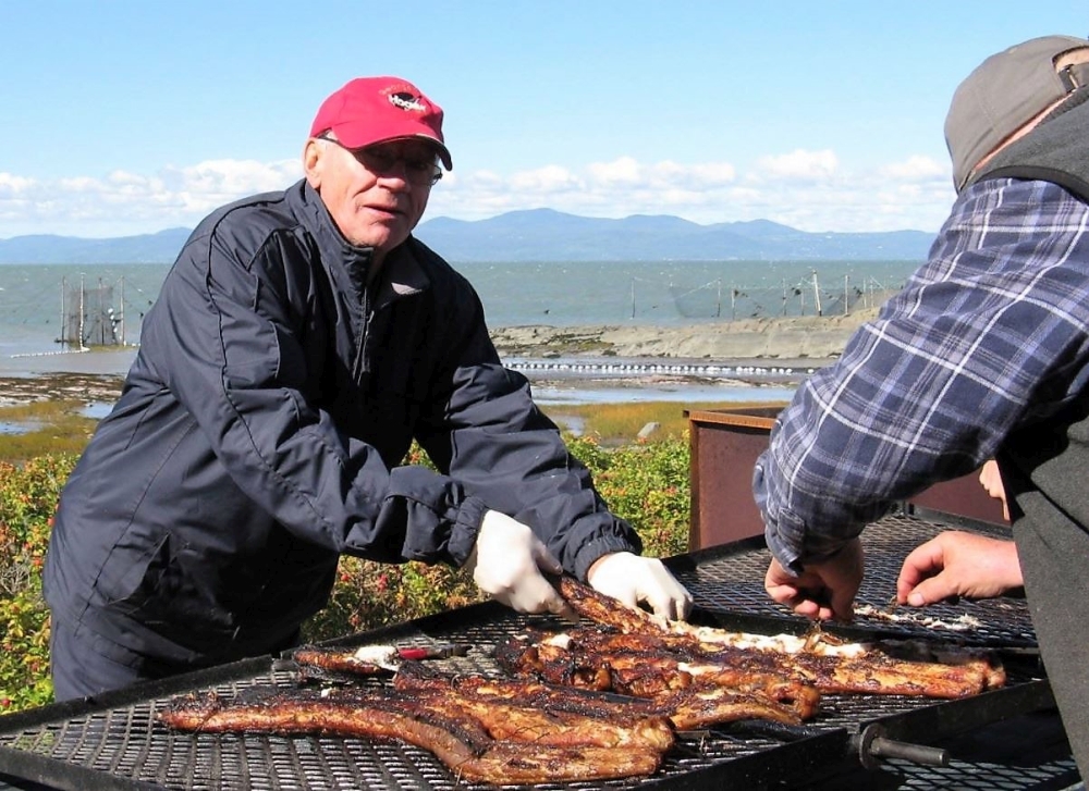 Two men grilling eel on a home-made barbecue next to the river.