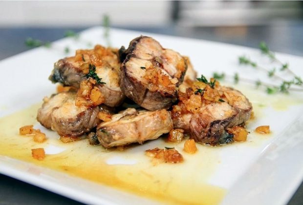 Slices of grilled eel with an orange peel sauce on a square plate.