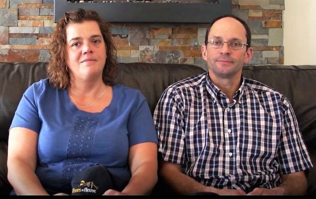 A couple sitting side by side on a brown leather couch.