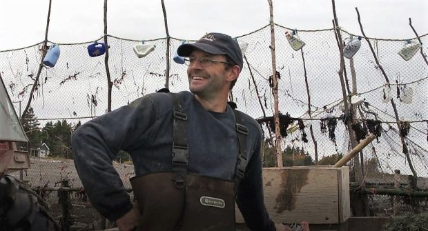 Head and shoulder view of a fisher with his right-hand on his hip, standing in front of the nets of his eel weir.