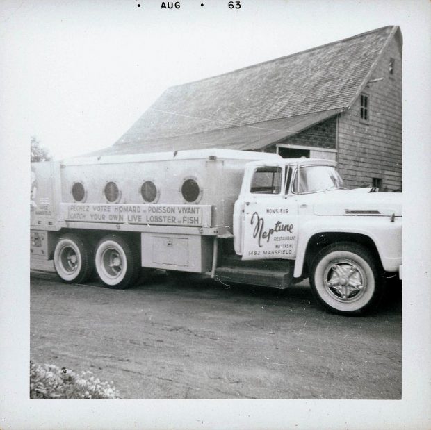 Tank truck used for transporting live fish. A sign on the side of the truck says: “Neptune Restaurant Montréal. Prenez votre homard et poisson vivant”. Black and white photograph.