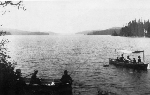 Black and white photo, two boats on sprawling lac Édouard. In the foreground, men fish in one boat, while further away women sit in the shade of a canopy built just for them.