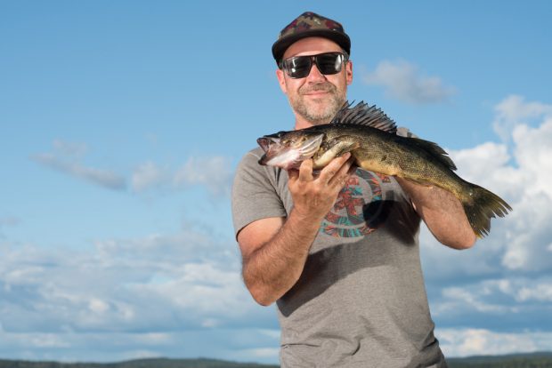 Colour photo, a man proudly holds a yellow walleye.