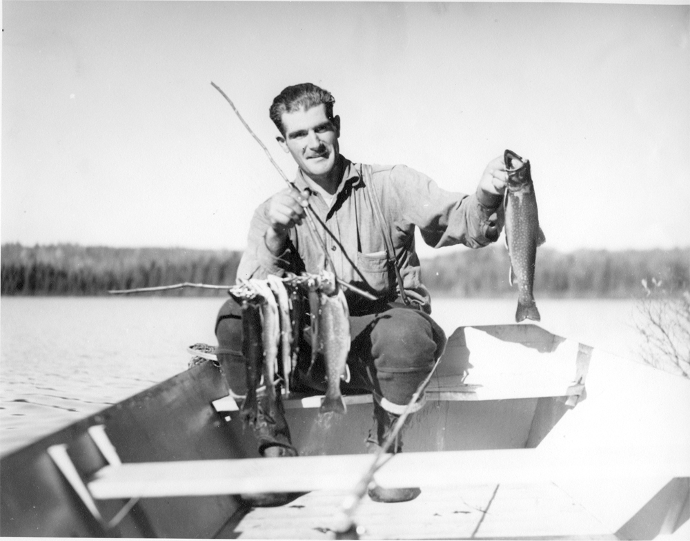 Photo en noir et blanc, un guide de pêche posant avec de belles truites mouchetées. Cet homme est assis dans une chaloupe.