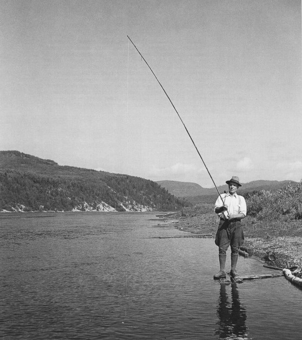 Black and white photo of a fisherman standing on the banks of the Saint-Maurice River.