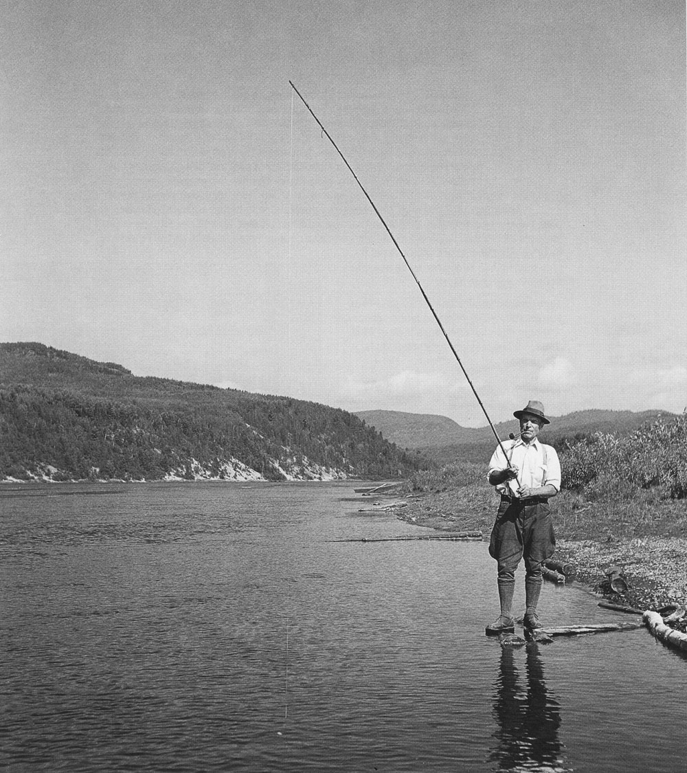 Black and white photo of a fisherman standing on the banks of the Saint-Maurice River.