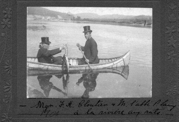 Black and white photo, two men in a birch bark canoe on a river.