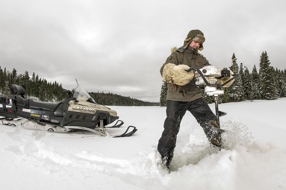 Colour photo, a man drills a hole on a frozen lake with the help of a gas ice auger.