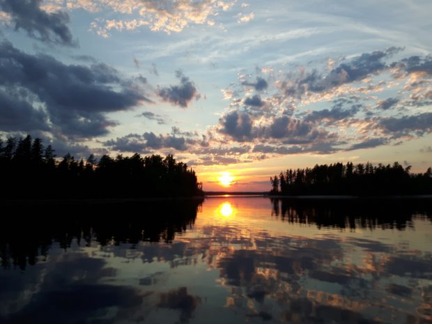 Colour photo of a sunset; the cloudy sky is reflected on the water’s surface.