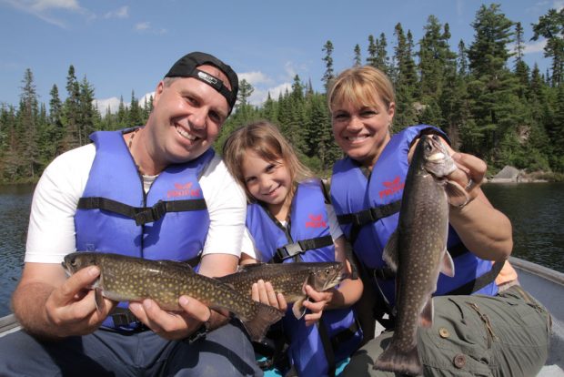 Colour photo, a family, father, mother and daughter, sitting in a rowboat, each holding a beautiful speckled trout