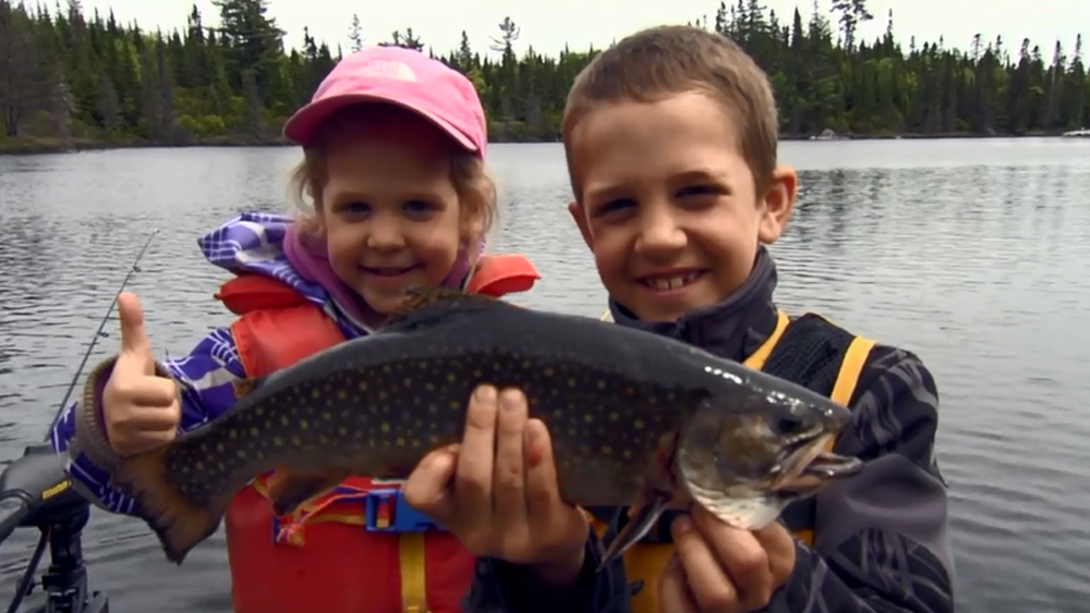 Two children, a boy and a girl proudly pose with a beautiful speckled trout in hand.