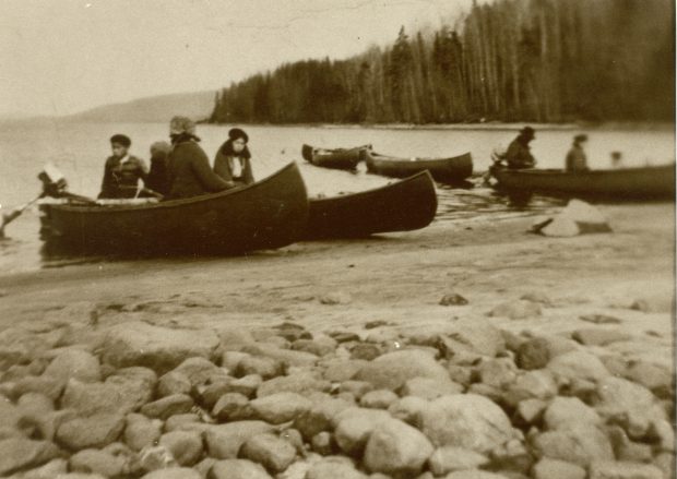 Black and white photo, a few canoes by the river’s edge. Everyone is ready to go fishing.