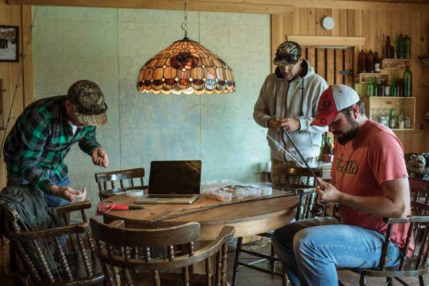 Colour photo, three men near a table preparing their rigging for a fishing trip.