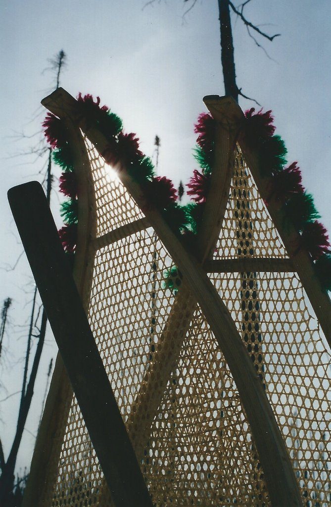 Raquettes décorées de petits pompons en laine, posées à la verticale dans un banc de neige.