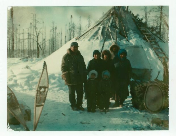 Seven people standing beside snowy teepee.