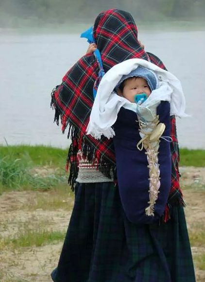 A woman with a shawl carries her baby on her back.her's back