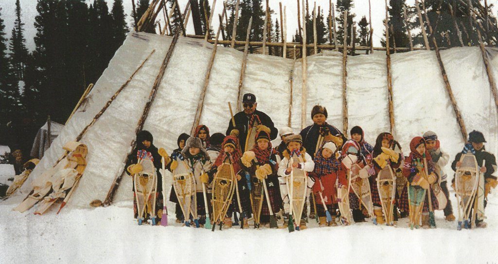 Group of 18 children hold their snowshoes in front of a tent made of poles and canvas