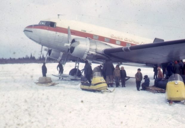 Prop plane on the ice surrounded by skidoos, sleds, and a group of men and children.