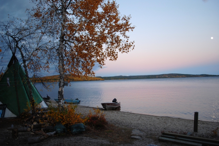 Tent, birch tree, and two motorboats by lake at sunset