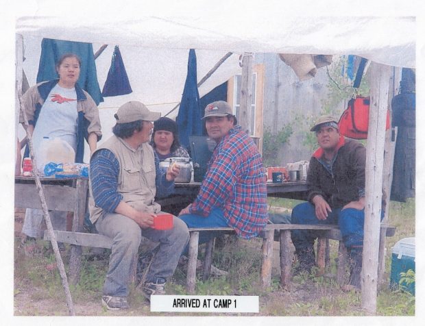 Three men wearing caps and two women at a picnic table